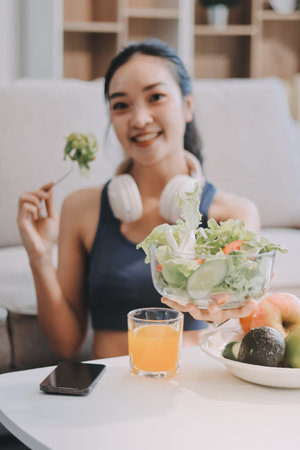Fit young Asian women in activewear sitting on yoga mat and eating fresh vegetable salad after workout, representing clean eating, fitness lifestyle, wellness routine and health balance.の写真素材