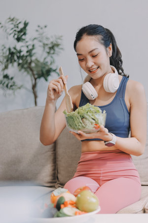 Fit young Asian women in activewear sitting and eating fresh vegetable salad after workout, representing clean eating, fitness lifestyle, wellness routine and health balance.の写真素材