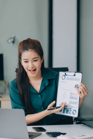 Determined asian businesswoman works in a modern office, confidently analyzing data on her clipboard, embodying success and professionalism with a smileの写真素材