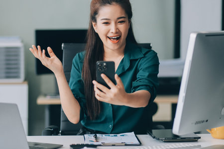 Determined asian businesswoman works late in a modern office, confidently analyzing data on her laptop, embodying success and professionalism with a smileの写真素材