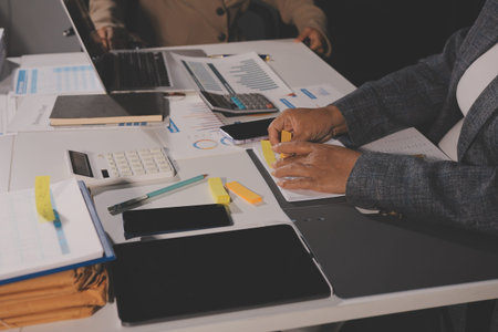 business documents on office table with tablet, smart phone and laptop and two colleagues discussing...
