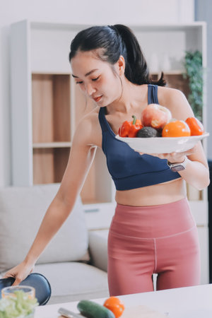 Fit young Asian women in activewear sitting on yoga mat and eating fresh vegetable salad after...