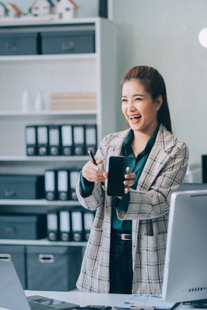 Determined asian businesswoman works late in a modern office, confidently analyzing data on her...
