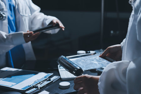Two doctors and a female nurse meet at a table in the hospital, collaborating on medical tasks using...