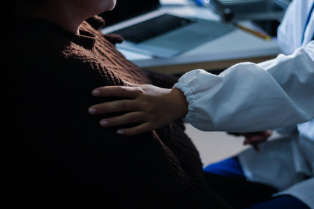 Senior patient lying in hospital bed receiving comforting touch from young female nurse, hands gently clasped together, medical care setting visibleの写真素材