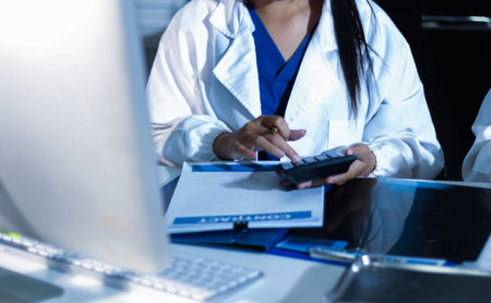 Medical team having a meeting with doctors in white lab coats and surgical scrubs seated at a table discussing a patients working online using computers in the medical industry.の写真素材