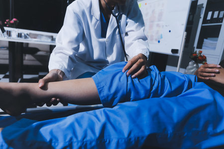 Asian male doctor examining foot of female patient sitting on bed in hospital room. Performing medical checkup. Diagnosing injury. Providing healthcare. Podiatry. Physical therapy. And rehabilitationの写真素材