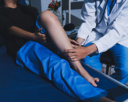 Asian male doctor examining foot of female patient sitting on bed in hospital room. Performing...