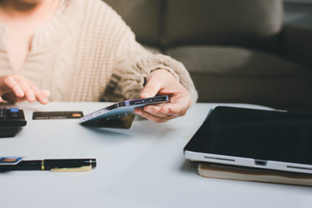Close up cropped man use laptop pc computer hold credit card speak on cell phone sit at table in coffee shop cafe relax rest in restaurant in free time indoor Freelance mobile concept Focus on objectの写真素材