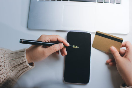 Close up cropped man use laptop pc computer hold credit card speak on cell phone sit at table in coffee shop cafe relax rest in restaurant in free time indoor Freelance mobile concept Focus on objectの写真素材