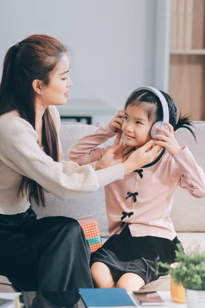 A cheerful Asian mother helps her young daughter do homework and color a book at home, while the...
