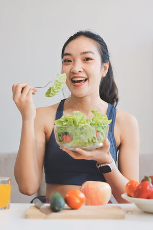 Fit young Asian women in activewear sitting on yoga mat and eating fresh vegetable salad after workout, representing clean eating, fitness lifestyle, wellness routine and health balance.の写真素材