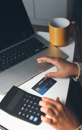 Close up cropped man use laptop pc computer hold credit card speak on cell phone sit at table in coffee shop cafe relax rest in restaurant in free time indoor Freelance mobile concept Focus on objectの写真素材