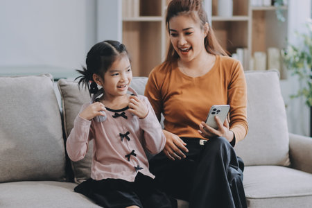 A cheerful Asian mother helps her young daughter do homework and color a book at home, while the...