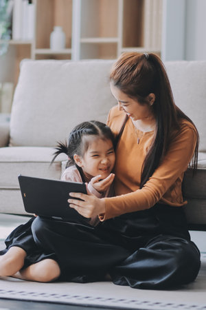 A cheerful Asian mother helps her young daughter do homework and color a book at home, while the...