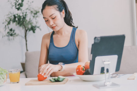 Fit young Asian women in activewear preparing fresh vegetable salad, representing clean eating,...