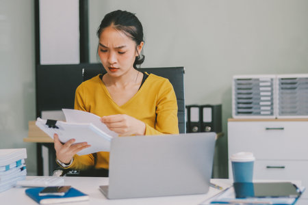 Young professional woman suffering from headache while analyzing financial charts and graphs on...