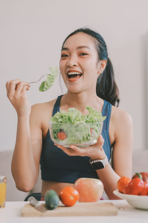 Fit young Asian women in activewear sitting on yoga mat and eating fresh vegetable salad after workout, representing clean eating, fitness lifestyle, wellness routine and health balance.の写真素材