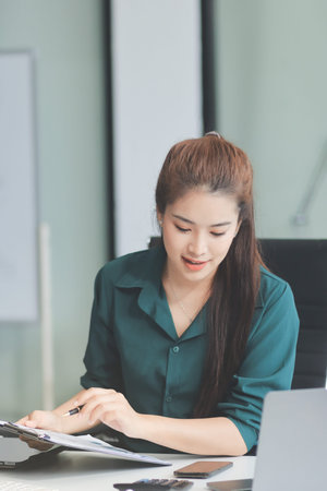 Determined asian businesswoman works late in a modern office, confidently analyzing data on her...