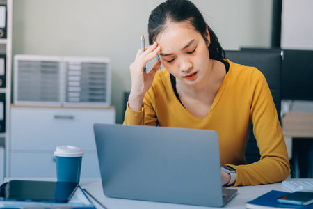Young professional woman suffering from headache while analyzing financial charts and graphs on...