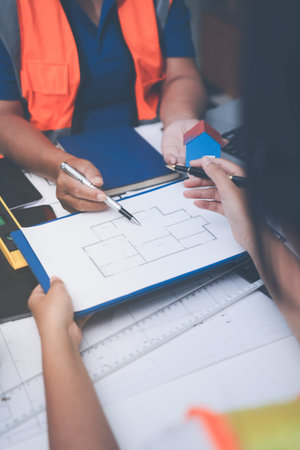 engineer and an architect reviewing blueprints and construction plans together at a bustling...