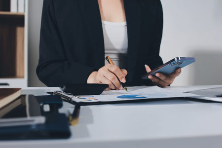 Auditors collaborating in modern office, analyzing financial documents and using calculator with a laptop displaying charts. Audit and taxes in businessの写真素材