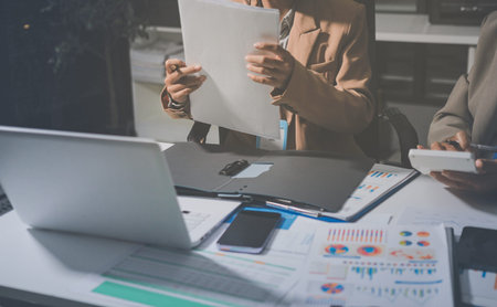 Business colleagues analyzing financial charts and reports on the table while having a focused discussion about strategies and market performance during an important meeting in a modern office setupの写真素材