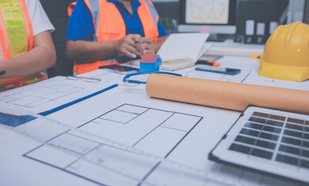 engineer and an architect reviewing blueprints and construction plans together at a bustling...