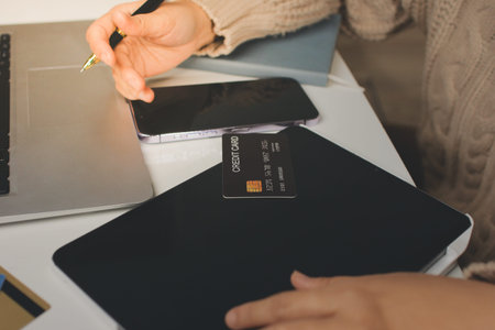 Close up cropped man use laptop pc computer hold credit card speak on cell phone sit at table in...
