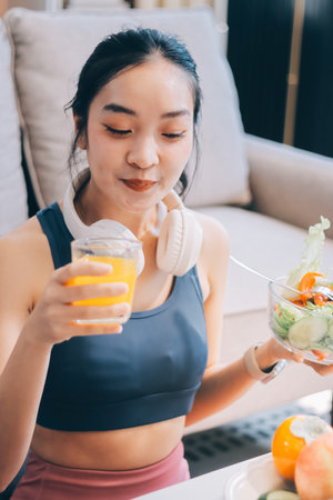 Fit young Asian women in activewear sitting on yoga mat and eating fresh vegetable salad after workout, representing clean eating, fitness lifestyle, wellness routine and health balance.の写真素材