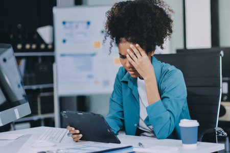 Tired business woman in stress works at a laptop while sitting at a table at home and holds her hand...