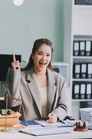 Confident Lawyer Working at Desk: A young Asian female lawyer confidently works on her laptop,...