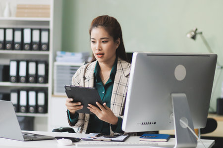 Determined asian businesswoman works late in a modern office, confidently analyzing data on her...