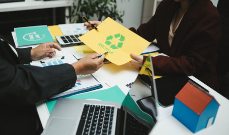 Corporate team discussing ESG goals and clean energy strategies in conference room, reviewing sustainable supply chain documents and laptop presentation, business sustainability