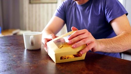 A man is opening a box of food on a table during his breakfastの写真素材