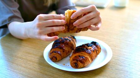 Hands of a woman is cuting a croissant on a tableの写真素材