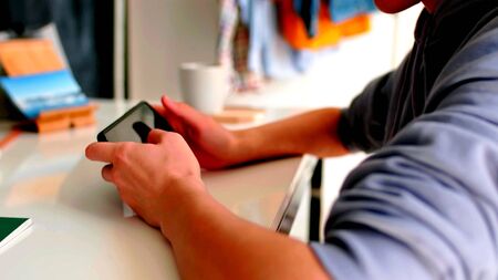 Arms of a young man who is using a smartphone on a tableの写真素材