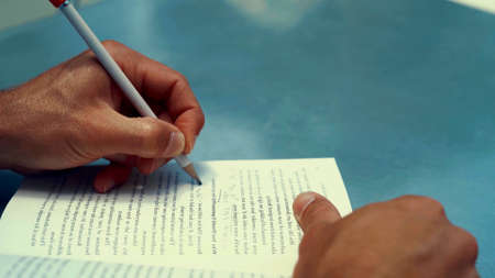 A photo of the hands of a black man who is writing on a book