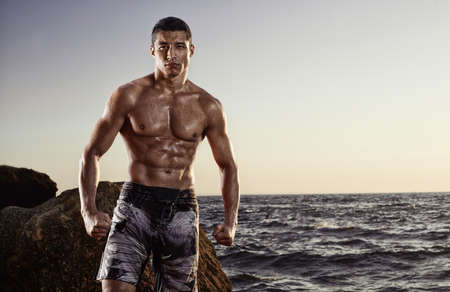 Handsome muscular young strong athlete on a beach background after workout. MMA, boxing fighter, wrestler. Outdoor fitness trainingの写真素材