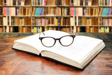 Open book with glasses on the desk against libraryの写真素材