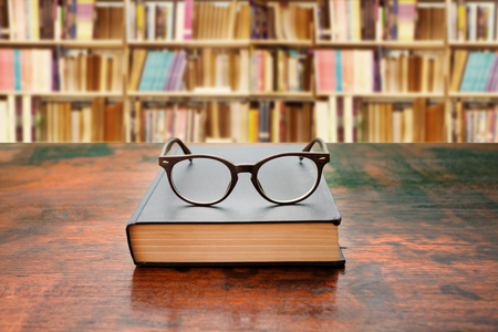 book with glasses on the desk against libraryの写真素材