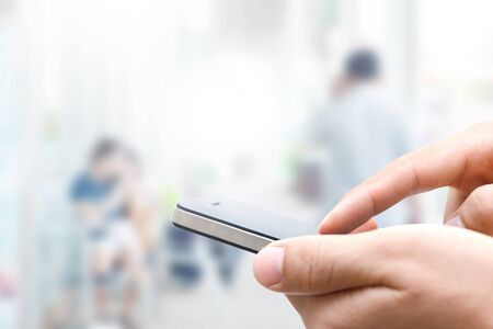 Closeup man hand using smart phone against blurred people backgroundの写真素材