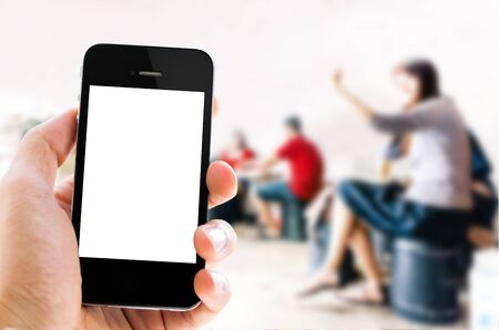 Close-up Hand holding white screen smart phone with blurred background of selfie people in restaurantの写真素材