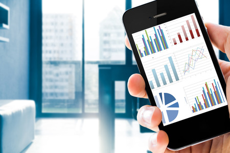 Closeup hand holding mobile phone show analyzing graph with conference room backgroundの写真素材