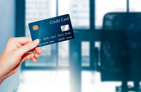 female  hand holding credit card against business office backgroundの写真素材