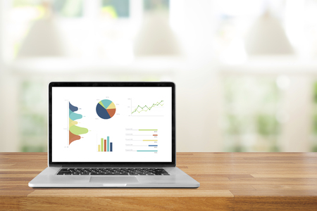 Laptop on wooden table showing charts and graph against modern background with green ourdoor view and lamp ,Analysis Business Accounting, Statistics Concept.の写真素材