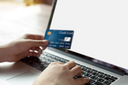 Woman hand holding blue credit card and using modern laptop, typing and texting. against defocus green nature outdoor.  mobile payment ,online shopping conceptの写真素材