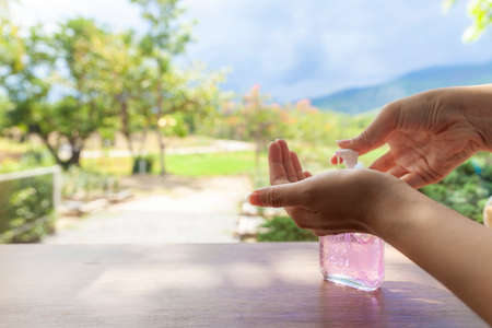 The beautiful hand of a woman pressing the alcohol gel with a backdrop of views of mountains and skyの写真素材