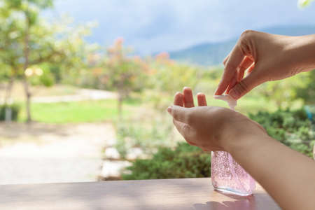 The beautiful hand of a woman pressing the alcohol gel with a backdrop of views of mountains and sky