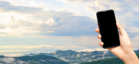 Female hand holding a smartphone with a blank screen on the background of the mountain landscapeの写真素材